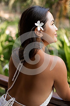 Close up vertical rearview captivating irresistible brunette woman with flower in hair striking pose, enjoying vacation