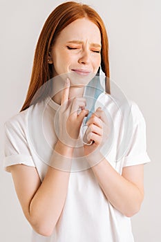 Close-up vertical shot of suffering young woman taking off disposable protective face mask, pointing finger to chin