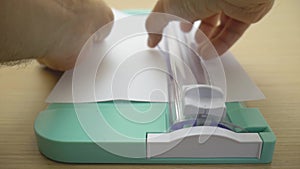 Close up video of a boy cutting a blank sheet of paper with a paper cutter mint on a wooden table