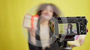 Close-up video camera screen with blogger advertising gifting and blurred young woman talking at yellow background