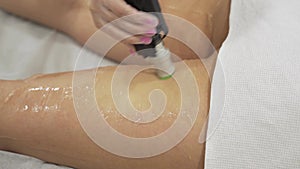 Close up video of professional cosmetologist doing laser hair removal of legs to young woman in beauty salon, Body care