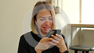 Close up video of smiling young woman sitting in cafe and typing on smartphone