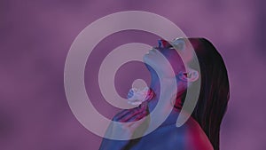 Close up video of a young woman touching her neck and shoulders with a pink rose in blue and pink color scheme and