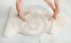 Close up view of 2 young girls sisters children standing with bare feet toes on very soft woolen sheepskin rug carpet.