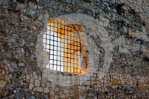 Close-up view of ancient stone defensive wall with big window and metal grill on it.  Kizkalesi castle is island medieval fortress