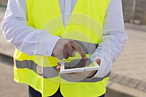 Close up view of an Architect or Engineer man hands using tablet on the construction site. Job concept. Wearing protective clothes