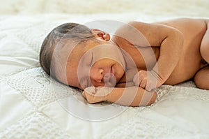 Close up view of Asian young newborn baby is sleeping and smile on white bed in the bedroom with soft light