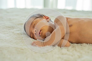 Close up view of Asian young newborn baby is sleeping and smile on white bed in the bedroom with soft light