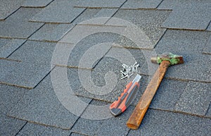 Close up view on asphalt bitumen shingles on a roof with hammer,nails and stationery knife background