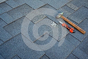 Close up view on asphalt bitumen shingles on a roof with hammer,nails and stationery knife background.