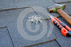 Close up view on asphalt bitumen shingles on a roof with hammer,nails and stationery knife background