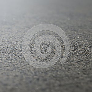 Close-up view of an asphalt or concrete surface. The texture is rough, with small,