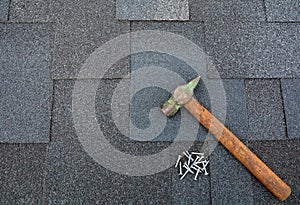 Close up view on asphalt roofing shingles background with hammer and nails.