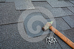 Close up view on asphalt roofing shingles background with hammer and nails.