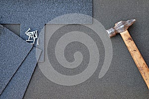 Close up view on asphalt shingles on a roof with hammer and nails background
