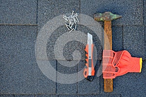 Close up view on asphalt shingles on a roof with hammer,nails and knife. Use of gloves in construction.