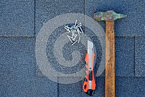 Close up view on asphalt shingles on a roof with hammer,nails and stationery knife