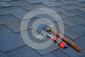 Close up view on asphalt shingles on a roof with hammer,nails and stationery knife background