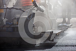 close-up view of asphalting paver machine during road street repairing works at day light with smoke and steam in the