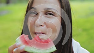 Close-up view of attractive cute brunette young woman with kind eyes, sniffing and eating slice of watermelon and