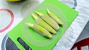 Close up view of baby corn on a green knife cutting board on a table at the kitchen