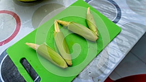 Close up view of baby corn on a green knife cutting board on a table at the kitchen