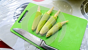 Close up view of baby corn on a green knife cutting board on a table at the kitchen