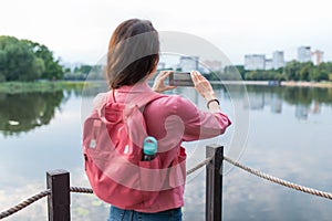 Close-up, a view from back, a girl in summer pond of river lake, records video and photos on a smartphone. Sightseeing