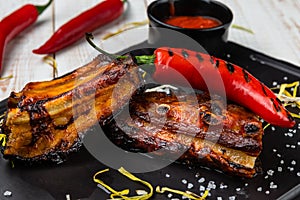 Close-up view baked pork ribs with chili sauce on a black board, lunch menu of national food restaurant served on white wooden