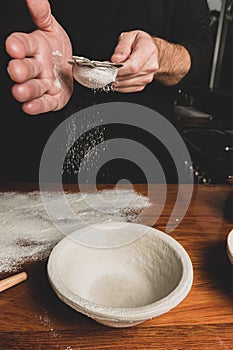 Close up view of baker sifting flour onto wooden bench