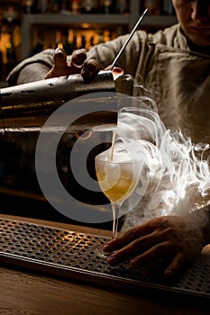 Close-up view of barman pouring steaming drink from shaker cup into wine glass