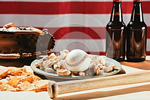 close-up view of baseball ball on plate with peanuts, bat and beer bottles, leather glove