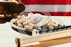 close-up view of baseball bats, baseball ball on plate with peanuts and leather glove on wooden table with us