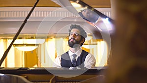 Close up view of bearded pianist playing the fortepiano enjoying the virtuoso music reflected in the piano cover