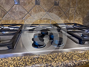 Close up view of a beautiful gas stove top with black knobs against a square tiled backsplash