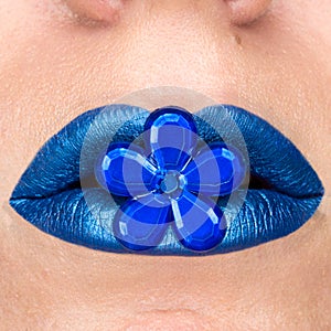 Close up view of beautiful woman lips with blue lipstick. Closed mouth. Cosmetology, fashion makeup. Jewellery flower