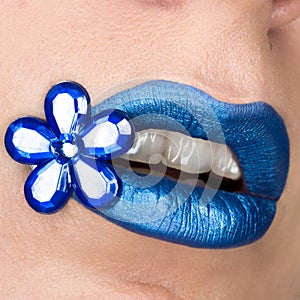 Close up view of beautiful woman lips with blue lipstick. Open mouth. Cosmetology, fashion makeup. Jewellery flower