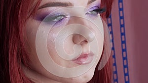 Close-up view of beautiful young girl model with bright red hair and purple makeup posing in the studio