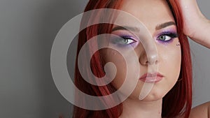 Close-up view of beautiful young girl model with bright red hair and purple makeup posing in the studio