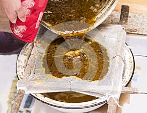 Close up view of beekeeper pouring melted beeswax cera alba through gauze filter to clean old used wax and reuse it.