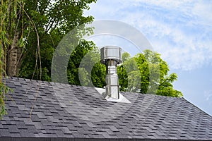 Close up view on bitumen asphalt roofing shingles and stainless steel chimney pipe.