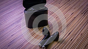 Close up view of black wireless bluetooth earphones or headphones and black box for storage and charging on wooden table