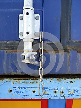 A close up view of a Blue container truck door lock. Rusty truck door latch with old chain. Grunge secured and Locked truck doors