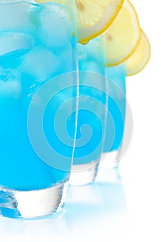 Close up view of blue lagoon cocktails with ice cubes on white