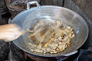 Close-up view of blurred motion of a female cook\'s hand holding a spatula to stir-fry pork