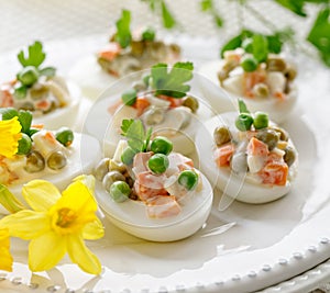 Close up view of boiled eggs stuffed with mayonnaise and vegetable salad served on a white plate.