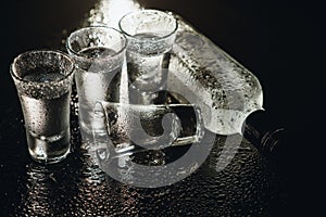 Close-up view of bottle and glasses of vodka standing isolated on black.