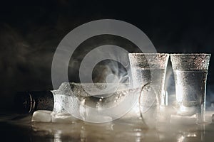 Close-up view of bottle and glasses of vodka standing isolated on black.