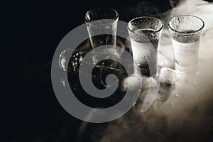 Close-up view of bottle and glasses of vodka standing isolated on black.