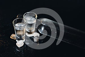 Close-up view of bottle and glasses of vodka standing isolated on black.